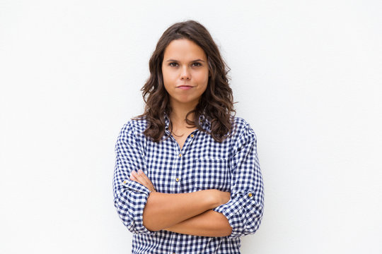 Positive determined student girl with arms crossed and funny grimace looking at camera. Young woman in casual checked shirt standing isolated over white background. Human emotion concept