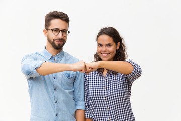 Happy united couple making fist bump gesture. Young woman in casual and man in glasses standing...