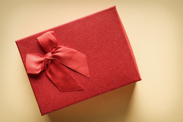 Close-up of a red gift box with a ribbon tied with a bow on a yellow background: concept of gift and romantic relationship