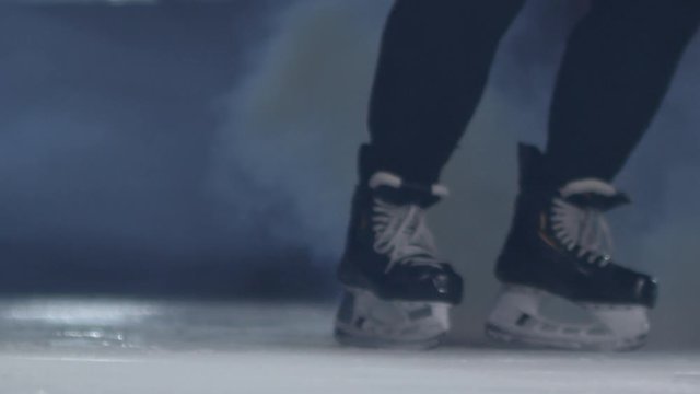 Close up legs of unrecognizable hockey player skating towards camera and splashing snow on ice rink