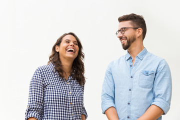Positive funny guy making his girlfriend laugh. Young woman in casual and man in glasses in glasses posing isolated over white background. Having fun together concept