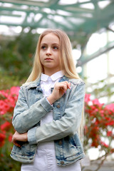 young girl with long white hair in a hat and a denim jacket walks in the garden with blooming azalea