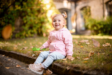 Smiling little girl playing with yellow fallen leaves sitting on the border