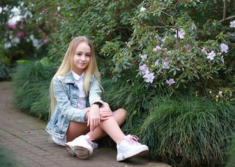 young girl with long white hair and a denim jacket is relaxing in the garden with blooming azalea