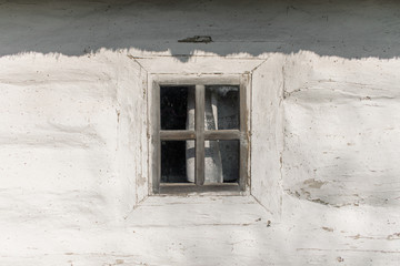 Window of an old rustic clay house. Wall of a white rural house with one window