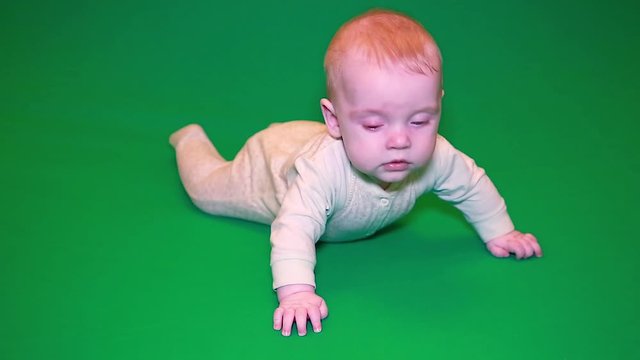 A newborn baby boy trying to crawl on the floor on a green screen . The concept of family happiness. Isolate the chroma key