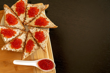 Spoon and plate of black bread with red caviar on dark table background with copy space. Red caviar sandwiches. Healthy food.