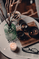 Cozy corner in the living room. Cozy warm blanket. Winter time. Candles on the table. Scandinavian interior decor. Cold winter time. Grey chair, throw blanket. Reading a book. Warm and cozy home