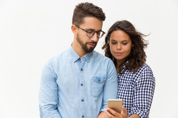 Focused couple reading message on cellphone screen. Young woman in casual and man in glasses in glasses posing isolated over white background. Mobile phone using concept