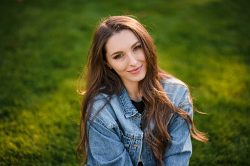 Portrait of a beautiful woman sitting on the green grass in the autumn park