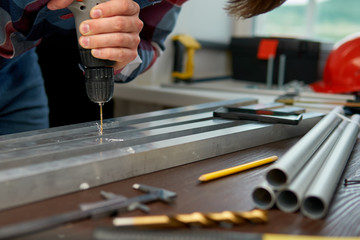 Close-up of a man in a plaid shirt, using an electric drill, drills a hole in an aluminum profile.