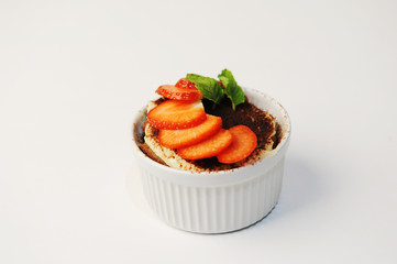 Tiramisu dessert in white bowl. Decorated with strawberry slices and mint leaves. White background, isolated