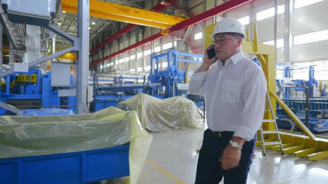 Businessman Business Owner In Hard Hat Walking Through Heavy Industry Manufacturing Plant Facility Talking About Project By Smartphone