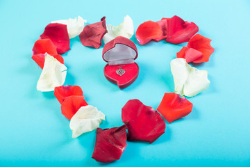 Heart of rose petals on a blue background and a heart-shaped box with jewelry.