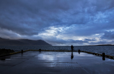 A person standing at Gledivik Bay looking at the dramatic stormy sky ahead, Djupivogur Village, East-Iceland