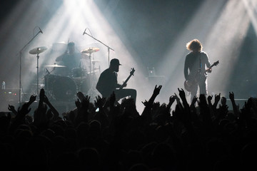 Concert shot, a huge crowd is standing in front of a lit stage clapping a band performance.