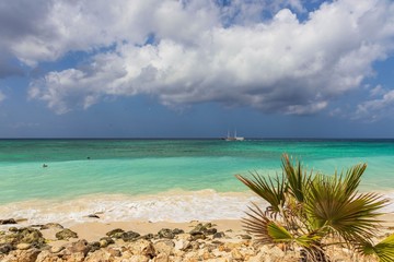Fototapeta na wymiar Gorgeous view of Atlantic ocean white sand coast line on turquoise water and blue sky with white clouds background. Small boat on horizon line.Eagle Beach of Aruba Island. 