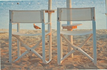 Beach scene at sunset with beach umbrella and white chairs