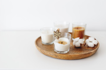 Obraz na płótnie Canvas Wooden tray with candles and cotton flowers standing on white table. Cozy home decoration. Interior decor. White background, copy space, selective focus.