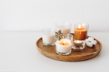Fototapeta na wymiar Wooden tray with burning candles and cotton flower standing on white table. Cozy home decoration, interior decor. White background, copy space, selective focus.