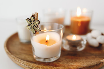 Wooden tray with burning candles standing on white table. Cozy home decoration, interior decor. White background, copy space, selective focus.