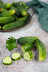 Fresh garden organic cucumbers and sprigs of parsley lie on a concrete background. Vertical photo