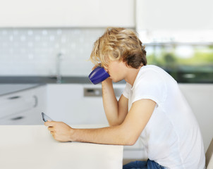 Fototapeta na wymiar Teenage boy typing text message.Sitting in the kitchen.Using smart phone