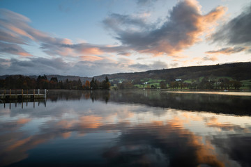 Stuning Autumn Fall sunrise landscape over Coniston Water with mist and wispy clouds
