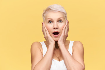 Studio shot of emotional excited middle aged Caucasian woman with blonde pixie hairstyle posing...