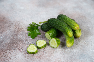 Fresh garden organic cucumbers and sprigs of parsley lie on a concrete background. Horizontal photo with copy space.