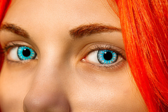A closeup of an eye with large, bright blue lenses. Eyelashes and pupil close-up. Red hair and eyebrows, soulful look.