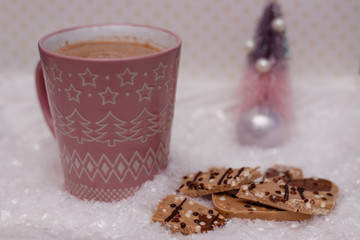 Pink cup of cocoa and chocolate in the snow.