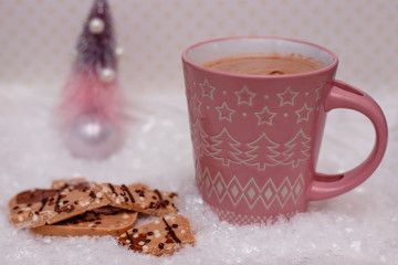 Pink cup of cocoa and chocolate in the snow.
