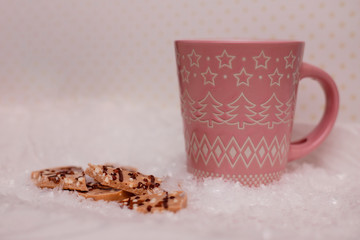 Pink cup of cocoa and chocolate in the snow.