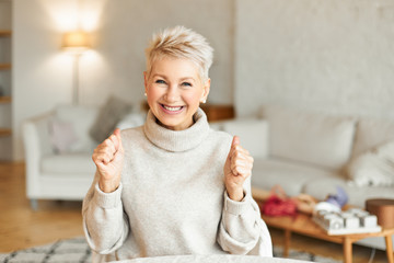 Positive human facial expressions and body language. Amazed attractive mature lady in cozy knitted jumper looking at camera with broad smile, winning lottery, excited with big sale prices or good news