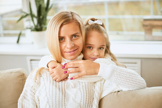 Happy holidays, Christmas and December concept. Close up image of blue eyed charming baby girl embracing beautiful young mother keeping arms around her neck, looking at camera with joyful smile