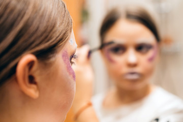 A teenager beautiful girl of 12 years paints white eyelashes by mascara in front of a mirror in the bathroom. DIY winter makeup for the Christmas New Year party. Closeup reflection portrait