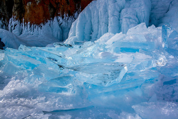 Transparent pieces of ice near the cliff on Lake Baikal. Beautiful blue color of ice. On the rock is red moss.