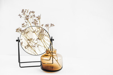 Branch flowers in a glass vase and mirror on white table. Decor for interior. Stylish decoration for home.
