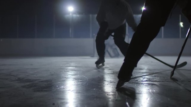 Legs of two unrecognizable hockey players skating on ice rink, one of them trying to score goal