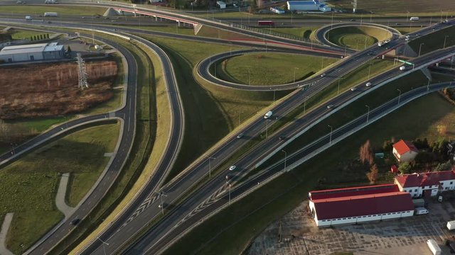 Aerial view of the intersection of highways on rough terrain (interchange) with ramps, heavy traffic, in rural areas. Poland.  Drone shot on a freeway with bridges and viaducts on a sunny evening.