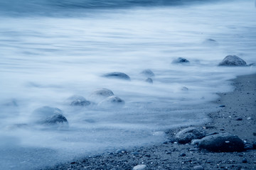 Fototapeta na wymiar Wave surf. Stones on the seashore. Classic Blue color 2020.