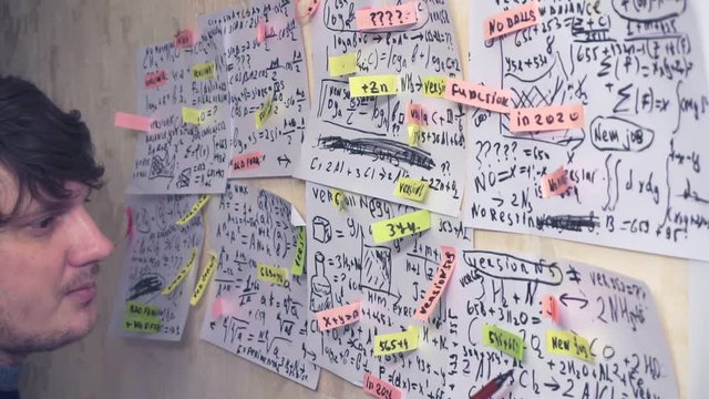 researcher works with various formulas and calculations on paper sheets that hang on the wall.research work.scientist in the workplace