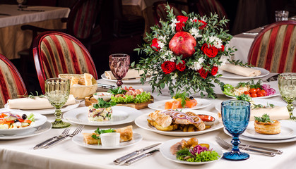 Served for holiday banquet restaurant table with grilled kebab meat, hot snack, dishes, salads, wine and water glasses. Table set for an event party in restaurant background