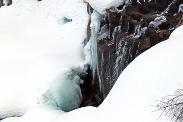 mountain stream flows among the rocks and puffy white snow on the banks