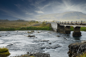 Obraz premium Landscape Iceland, a river is flowing under a bridge a road above it, fog in the background and a blue and white sky