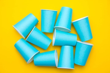 Many blue paper disposable cups on yellow background. Set for party. Top view. Minimalist Style. Copy, empty space for text