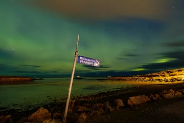 Foto op Aluminium Spectacular great, green, blue and orange northern lights above a lake in Bourganes, with reflection in the water, a signpost in the foreground, Iceland © Dasya - Dasya