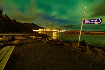 Foto op Aluminium Spectacularly beautiful green, blue and orange northern lights above a lake in Bourganes, with reflection in the water, a signpost right in the foreground, Iceland © Dasya - Dasya