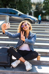 Fototapeta na wymiar Portrait of pretty young woman taking selfie photo on smartphone while sitting on stairs outdoors